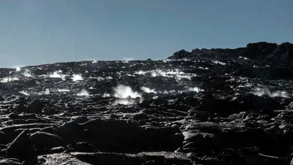 black steaming lava field under a blue sky